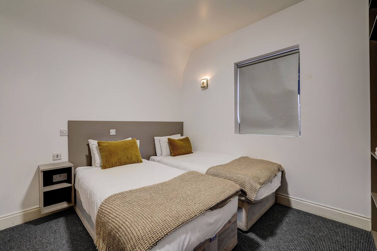 Une chambre d’hôtel avec deux lits, une table de chevet, une lampe fixée au mur et une fenêtre.