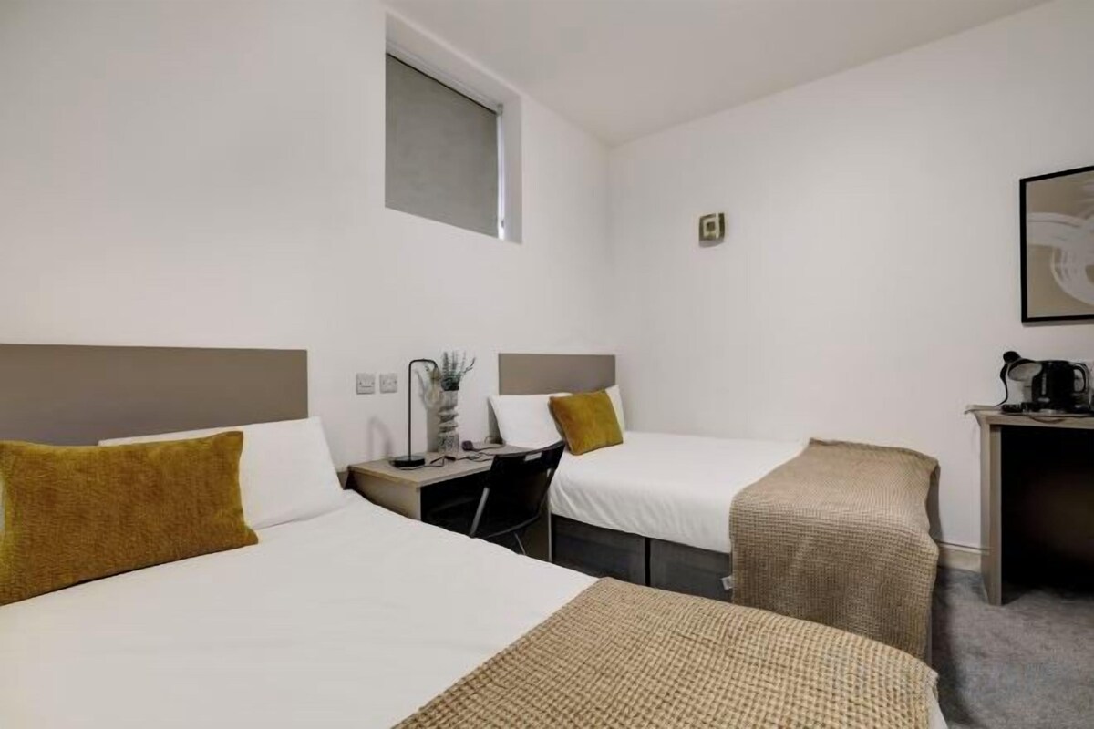 Ein Hotelzimmer mit zwei Betten, einem Schreibtisch, einem Sessel und einem kleinen Tisch mit Wasserkocher.