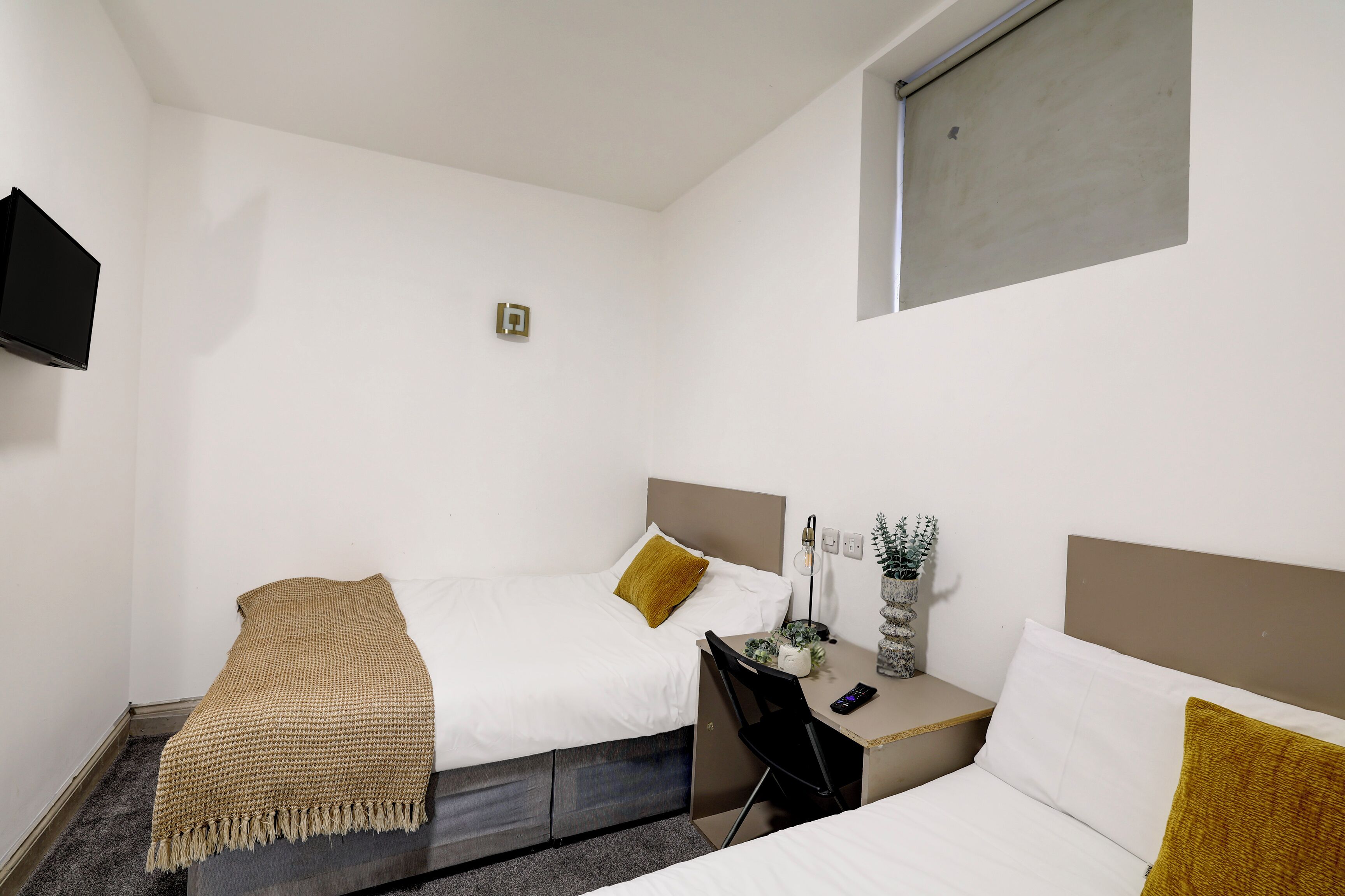 Ein kleines, modernes Hotelzimmer mit zwei Einzelbetten, einem Schreibtisch und einem Fernseher.