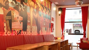 A restaurant with wooden tables and benches, a mural on the wall, and red curtains. - Ok Hostel Madrid (Madrid)