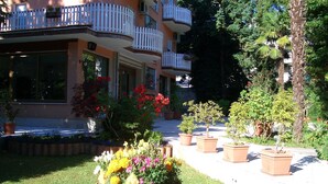 Un edificio de varios pisos con balcones, un jardín cuidado con plantas en macetas y un camino despejado que lleva a la entrada.