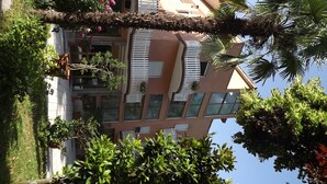 Un edificio de varios pisos con balcones, rodeado de exuberante vegetación y plantas florecientes.