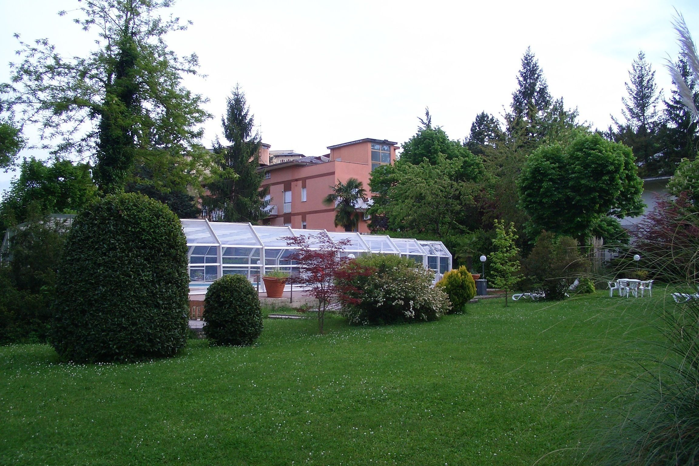 Ein Gewächshaus mit Glasdach, umgeben von gepflegten Rasenflächen und verschiedenen Bäumen.
