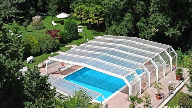 Piscina con cerramiento de vidrio, rodeada de vegetación exuberante y árboles.