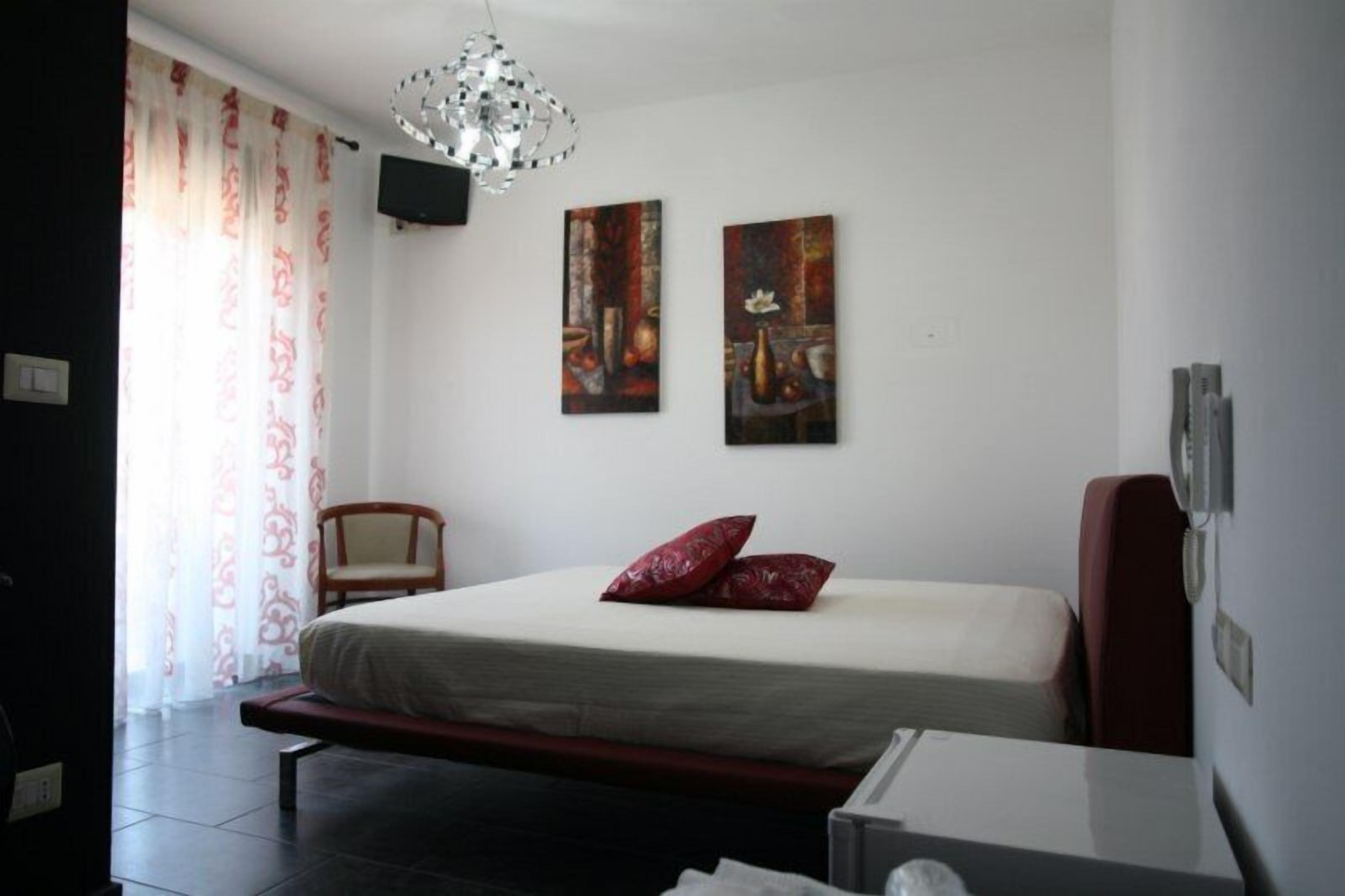 A bedroom with a bed, a chair, and two paintings on the wall.