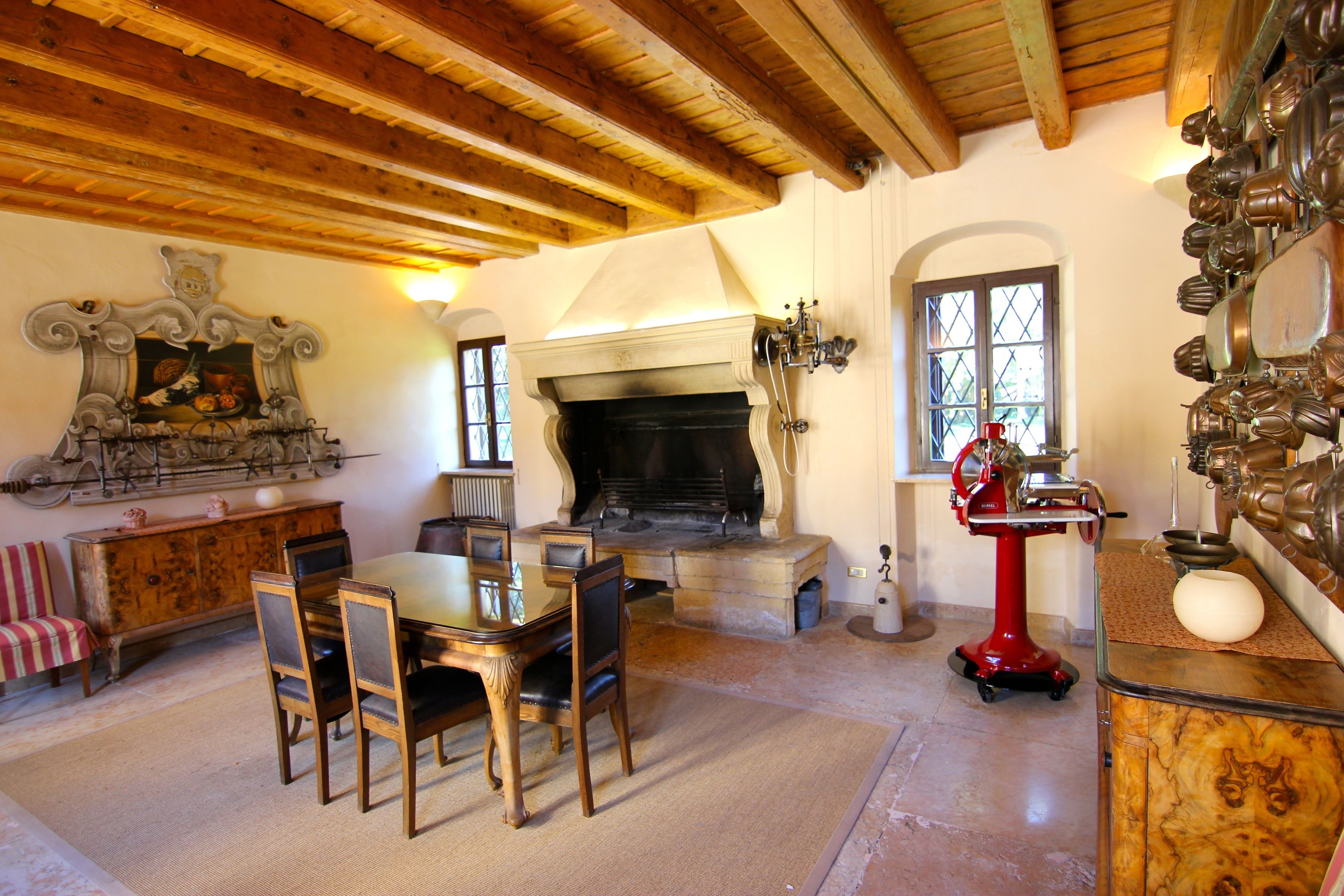 A dining area with a wooden table and chairs, a fireplace, and a collection of kitchen utensils on the wall.