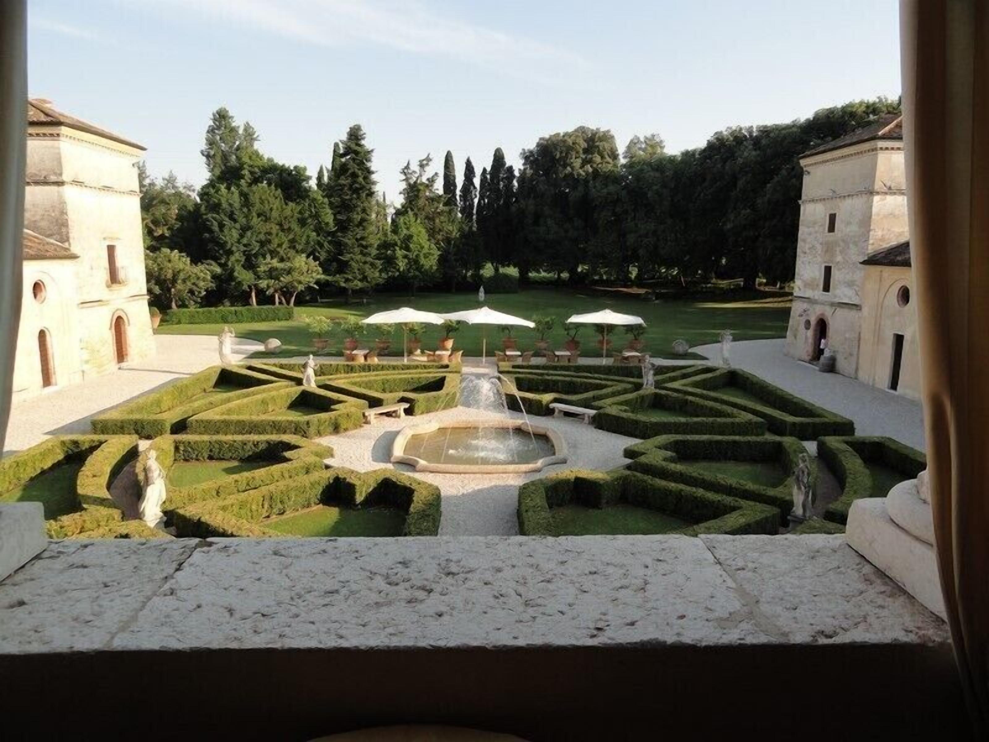 Un jardin à la française avec une fontaine centrale, des haies disposées de manière symétrique et des statues classiques.