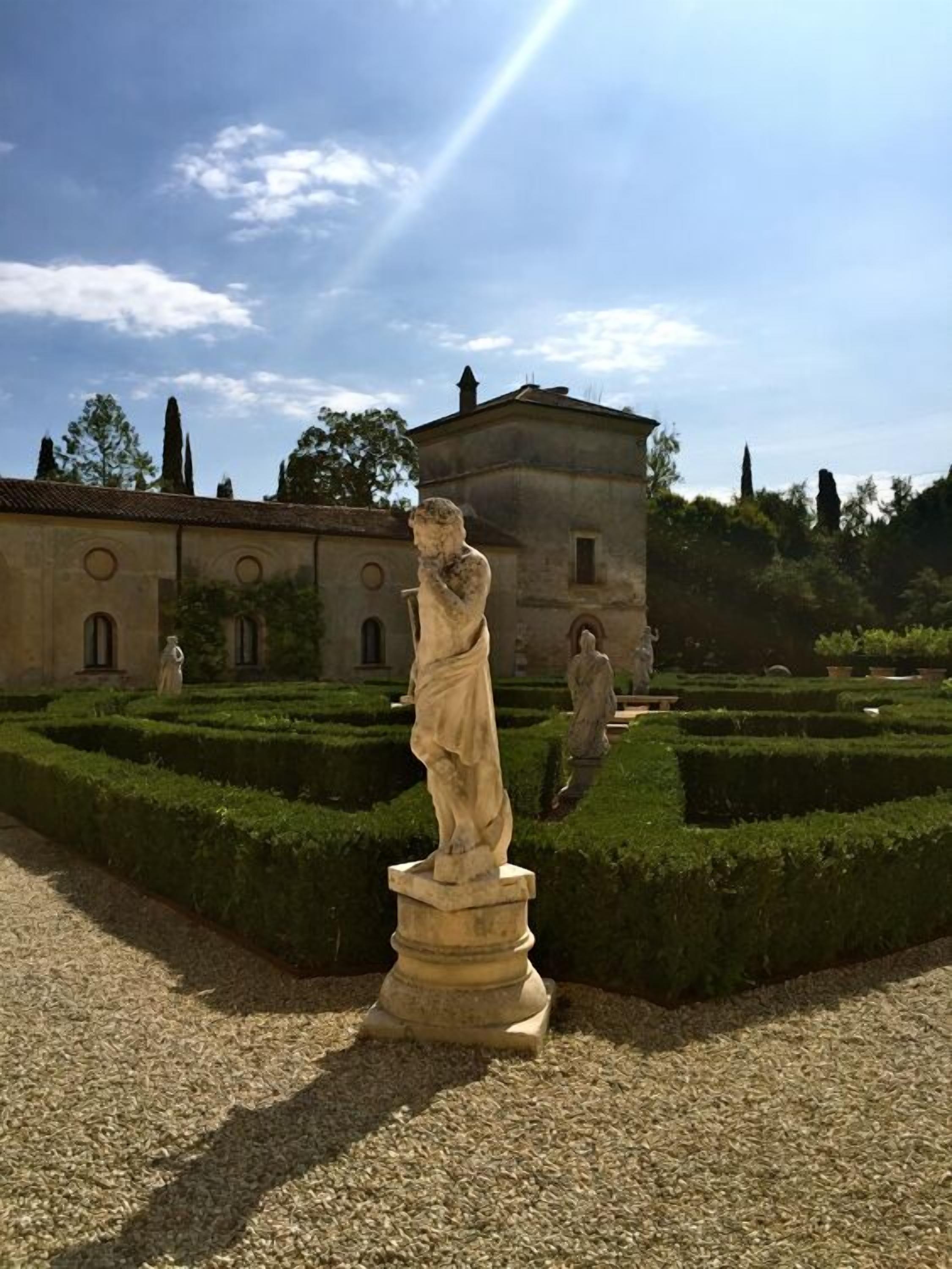 Una estatua en un jardín formal, con un edificio al fondo.