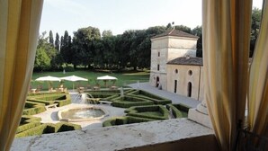 Vista de un patio con una fuente, setos cuidados y un edificio con ventanales de arco.