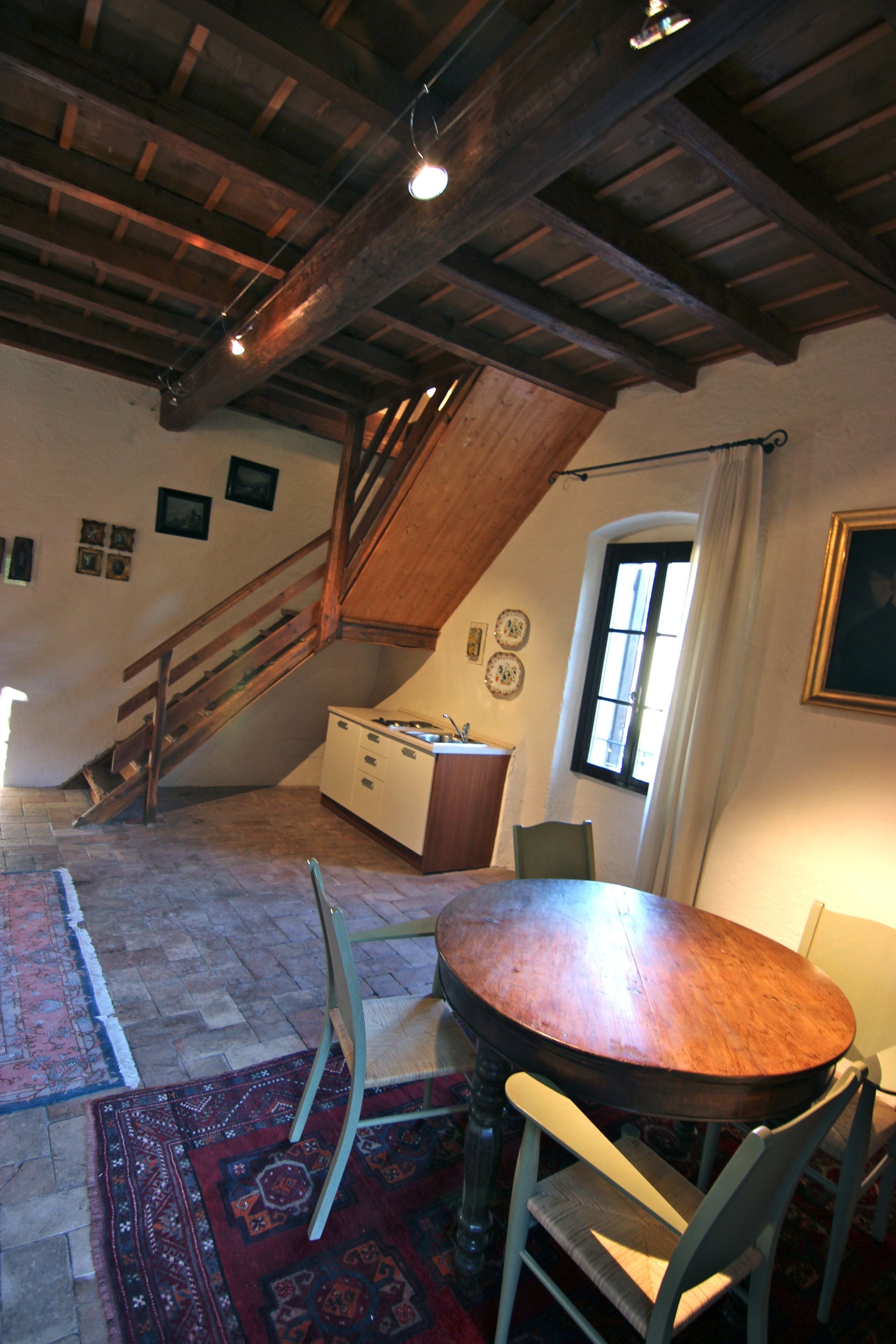 A dining area with a wooden table and chairs, a staircase, and a window with curtains.