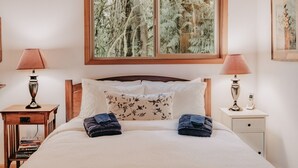 A neatly made bed with two towels, a wooden nightstand with a lamp, a bedside table with a lamp and a phone, and a window with a forest view. - 04sl- Hot Tub - Bbq - Pets Ok - Sleeps 5 1 Bedroom Home by RedAwning (Deming)