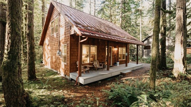 A wooden cabin with a porch, surrounded by tall trees. - 12gs - Bbq - Wifi - Dishwasher - Sleeps 4 2 Bedroom Home by RedAwning (Deming)
