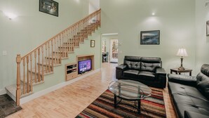 A living room with a wooden staircase, a black leather sofa, a glass coffee table, and a television. - 12gs - Bbq - Wifi - Dishwasher - Sleeps 4 2 Bedroom Home by RedAwning (Deming)