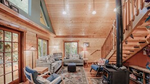 A cozy cabin interior with a wooden interior, a fireplace, and a large window overlooking a forest. - 21gs - Log  - Pets Ok - Sleeps 6 3 Bedroom Home by RedAwning (Deming)
