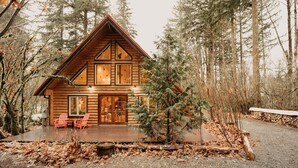 A log cabin with a wooden deck, large windows, and a red chair outside. - 21gs - Log  - Pets Ok - Sleeps 6 3 Bedroom Home by RedAwning (Deming)