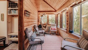 A cozy log cabin interior with a seating area, bookshelves, and large windows offering a view of the outdoors. - 21gs - Log  - Pets Ok - Sleeps 6 3 Bedroom Home by RedAwning (Deming)