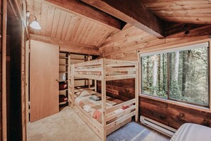 Relax in a cabin-style bedroom with a bunk bed arrangement and a large window offering a forest view.