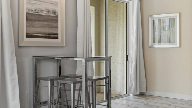 A room with a glass table and chairs, a sliding glass door, and two framed artworks on the walls. - Champions Gate Resort (Davenport)
