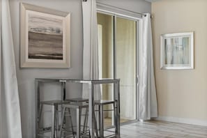 A modern room with a glass table and two bar stools, a sliding glass door, and two framed artworks on the walls. - Champions Gate Resort (Davenport)