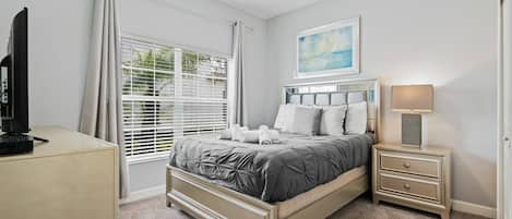 A bedroom with a bed, bedside tables, a desk, a TV, and a window with curtains.