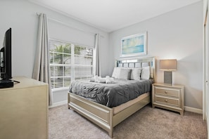 A bedroom with a bed, bedside table, and a TV on a cabinet. - Champions Gate Resort (Davenport)