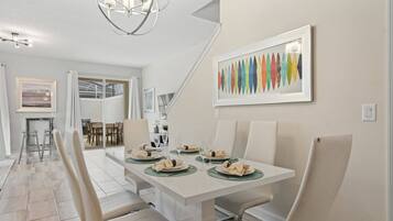 A dining area with a white table set for four, a chandelier, and a colorful abstract painting on the wall.
