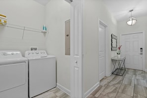 A laundry room with two front-loading washers and dryers, a shelf with towels, and a door leading to another room. - Champions Gate Resort (Davenport)