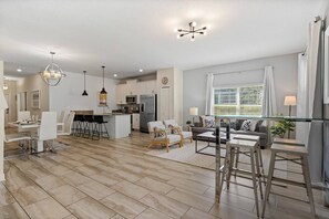 A modern kitchen with white cabinets, a stainless steel refrigerator, and a dining area with a white table and chairs. - Champions Gate Resort (Davenport)