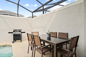 An outdoor patio with a table and chairs, a grill, and a pool. - Champions Gate Resort (Davenport)