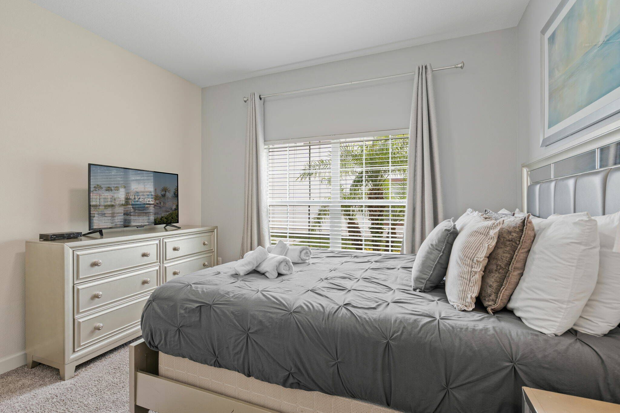 A bedroom with a bed, a dresser, a television, and a window with blinds.
