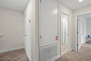 A hallway with white walls, a beige carpet, and a closed door with a vent. - Champions Gate Resort (Davenport)