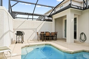 A backyard with a swimming pool, a barbecue grill, and a dining area with chairs and a table. - Champions Gate Resort (Davenport)