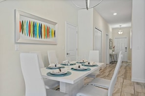 A dining area with a white table set for four, white chairs, and a colorful abstract painting on the wall. - Champions Gate Resort (Davenport)