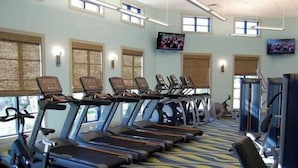 Une salle de sport équipée de tapis de course, de vélos d’exercice et d’un écran de télévision.