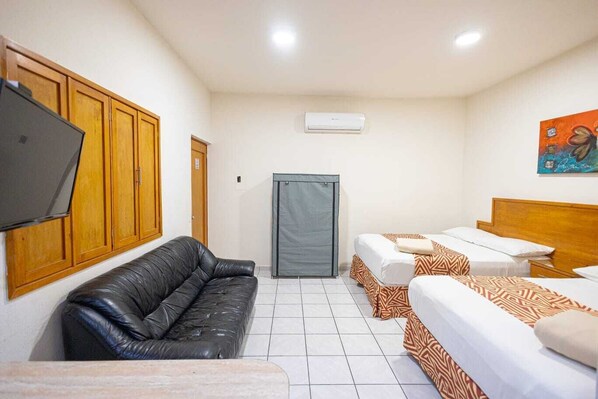 Habitación de hotel con sofá de cuero negro, dos camas individuales con ropa de cama estampada, una puerta gris y un aire acondicionado instalado.