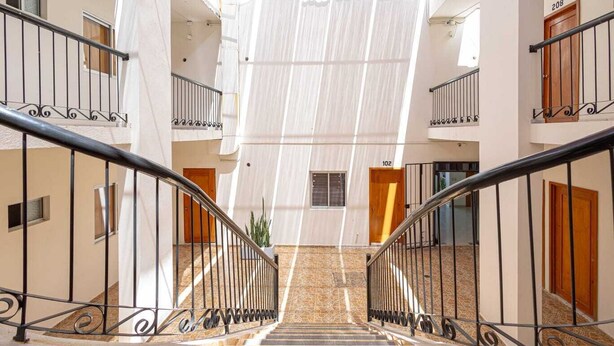 Un interior de varios niveles con una escalera central, paredes blancas y puertas de madera.