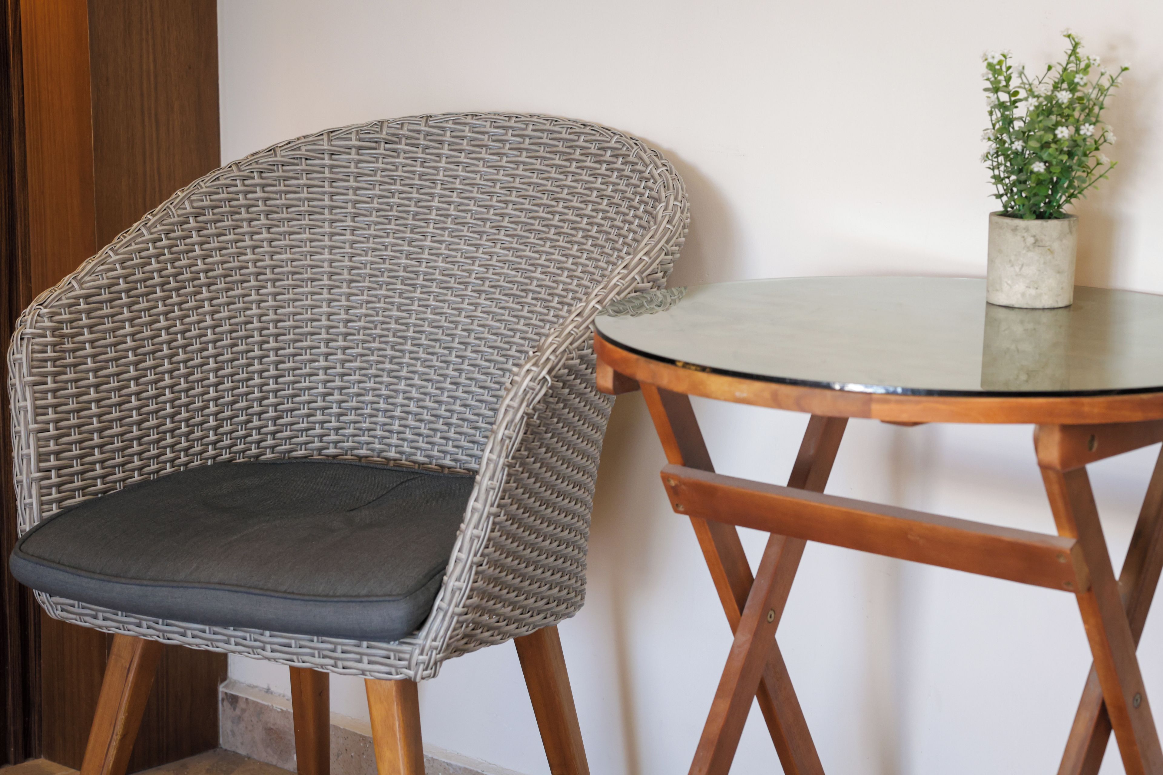 A wicker chair with a cushion and a small table with a potted plant.