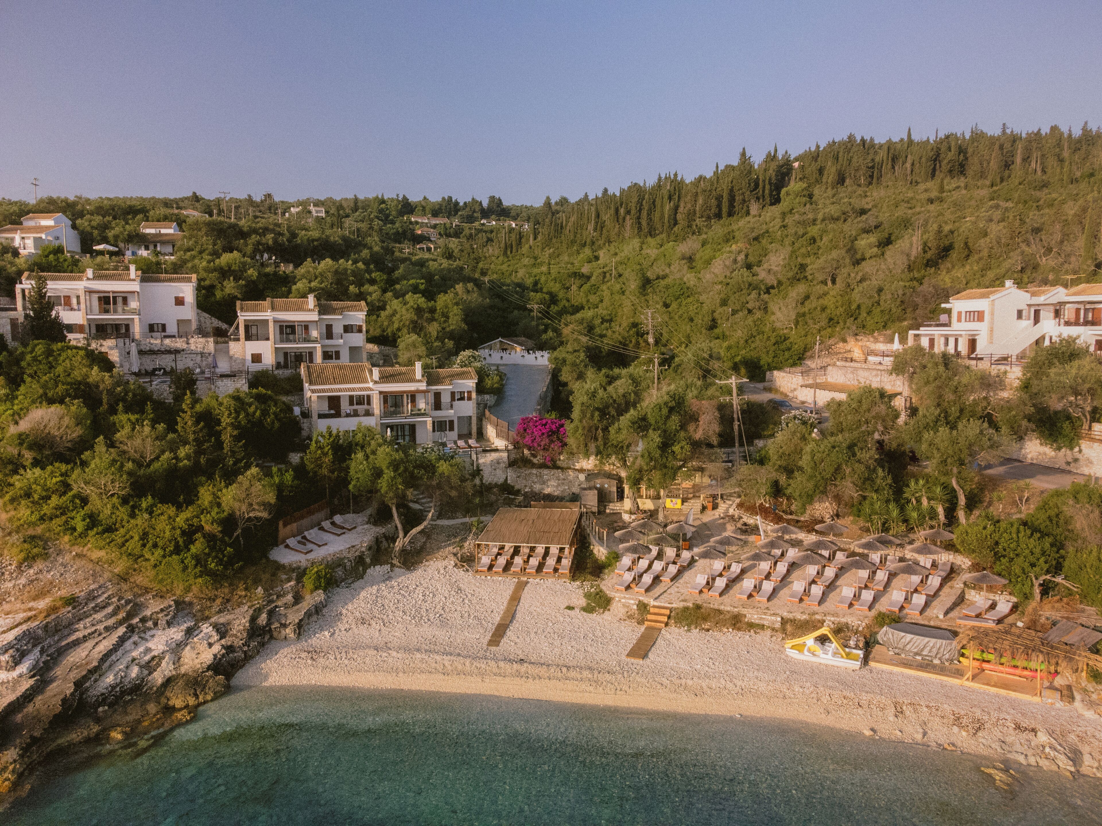 Una propiedad costera con varias construcciones, una playa y una ladera boscosa.