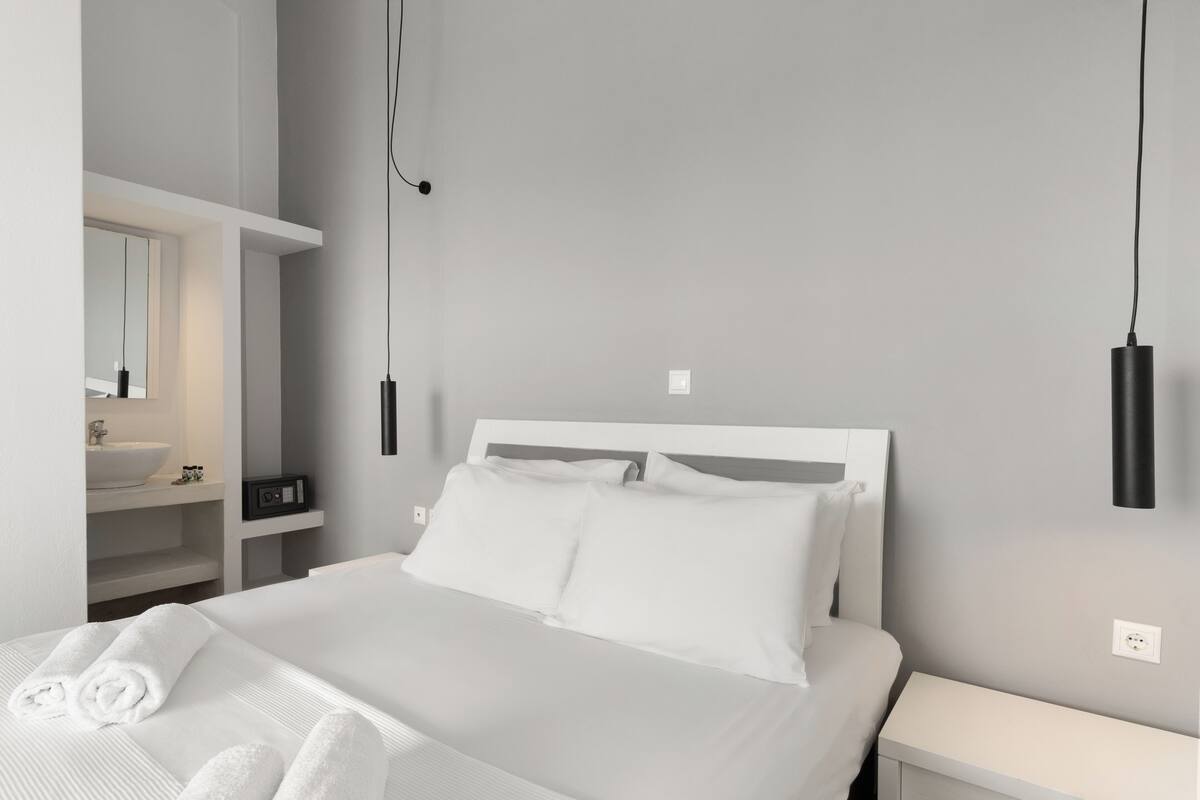 Ein modernes Hotelzimmer mit einem großen Bett, einem Nachttisch, einer integrierten Ablage mit Spiegel und einer Wandleuchte.
