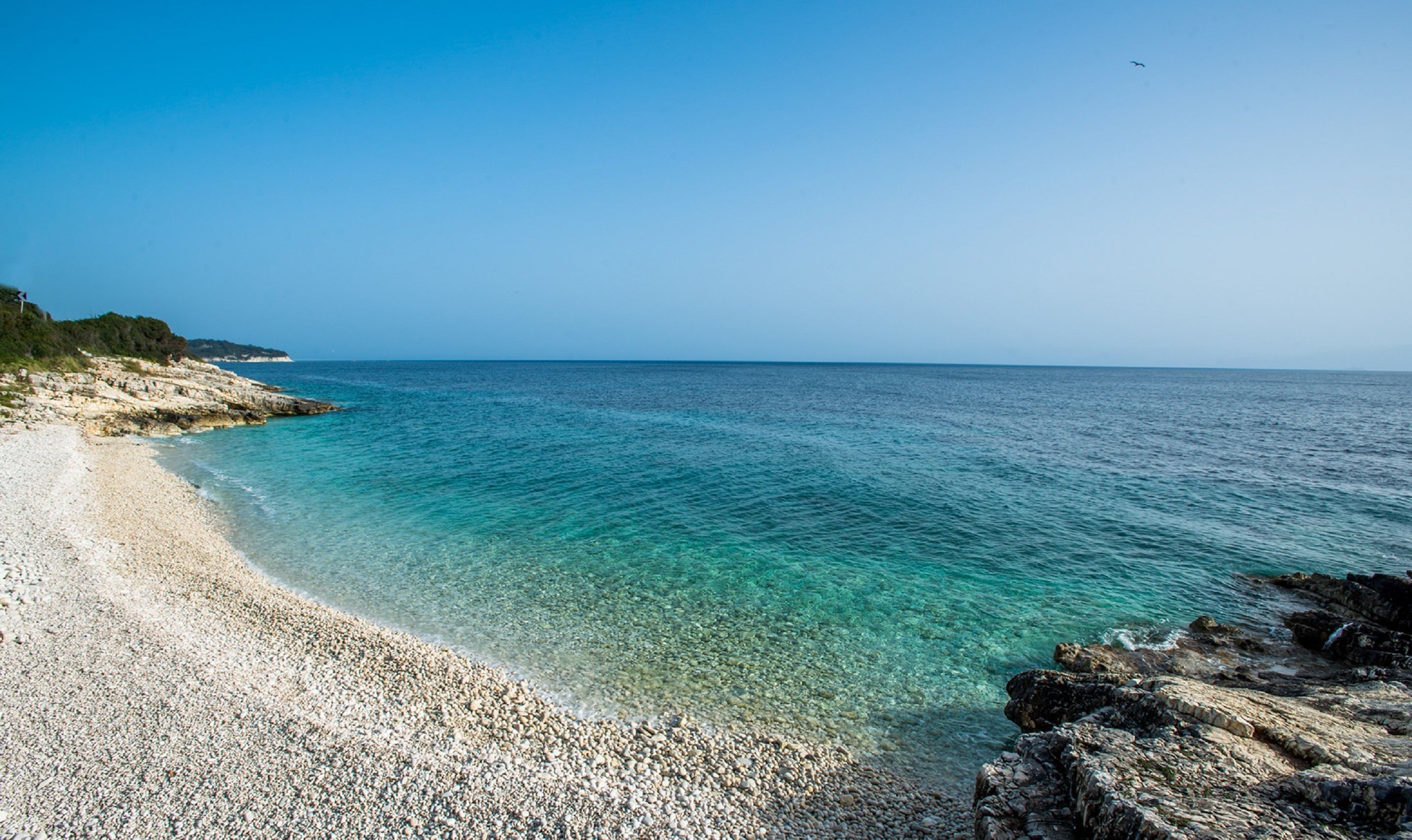 Een helder uitzicht op een kiezelstrand met rustig water en een veraf gelegen rotsformatie.