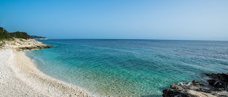 Een helder uitzicht op een kiezelstrand met rustig water en een veraf gelegen rotsformatie.