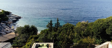 Ein Pool mit Meerblick, eine Lounge mit einer Couch und ein Strand mit Sonnenschirmen.