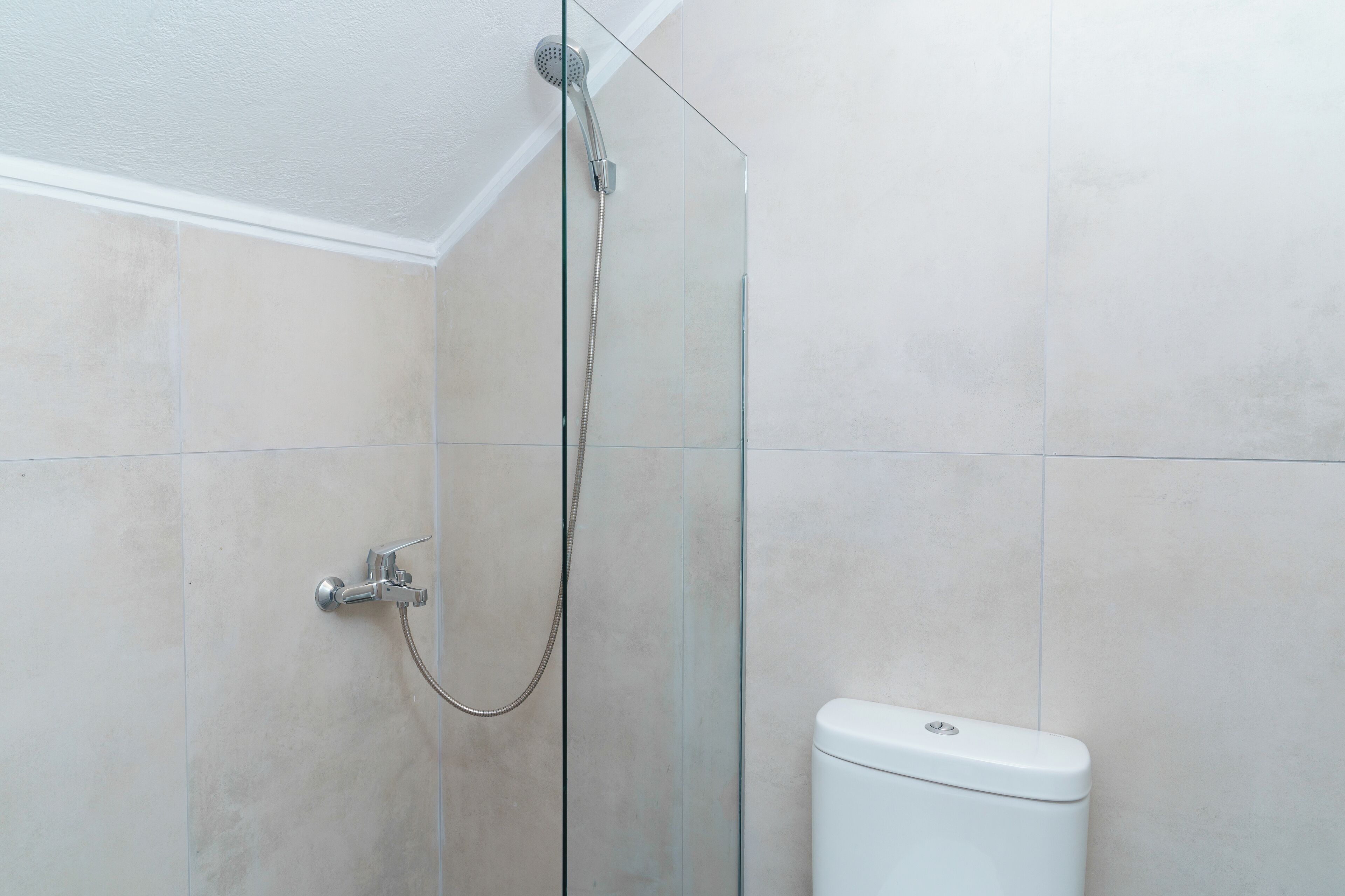 A modern bathroom with a glass shower enclosure, a white toilet, and beige tiled walls.