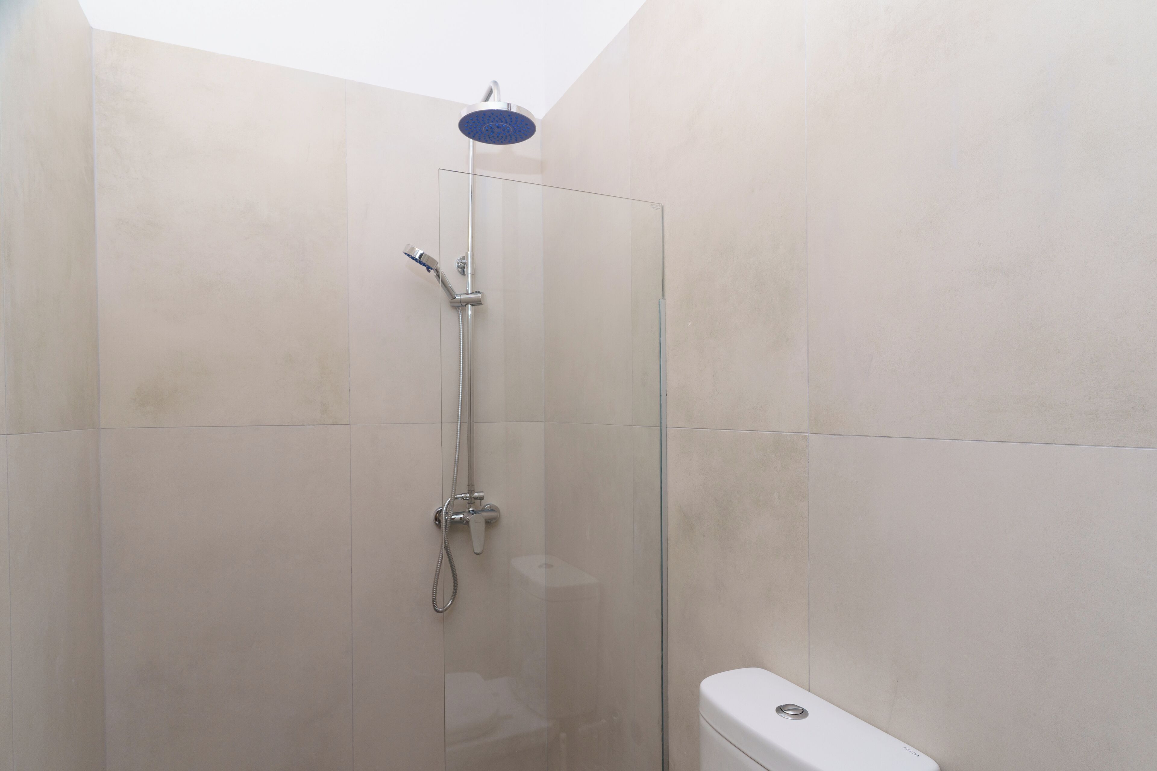 Une douche fermée par des parois en verre, dotée d’un pommeau de douche à main et d’un robinet mural.