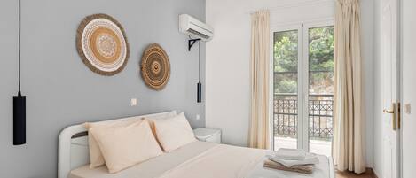 Un dormitorio ordenado con cama, mesitas de noche, equipo de aire acondicionado y vistas al exterior a través de una puerta corredera.