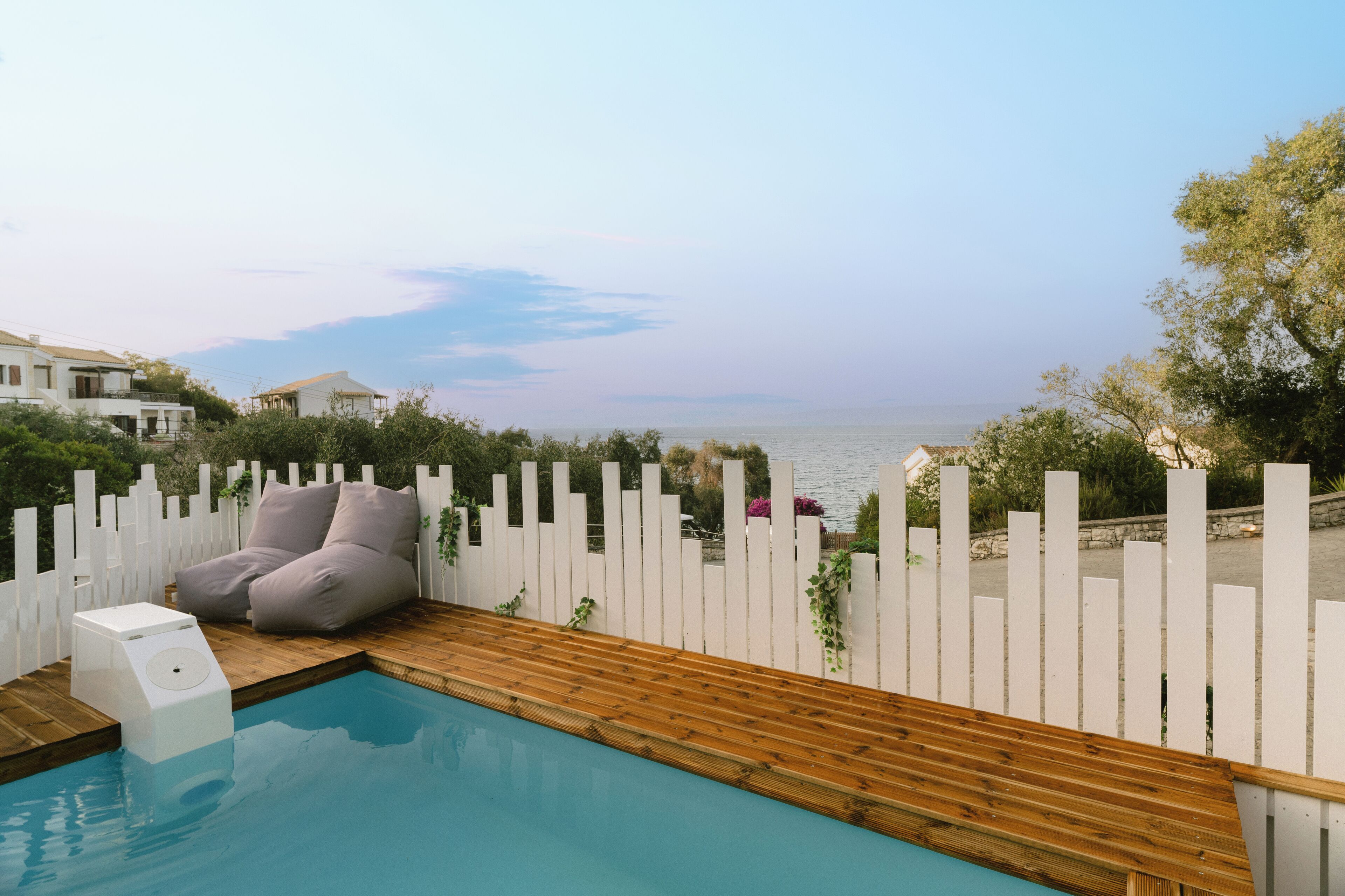 Zona de piscina con terraza de madera, valla blanca y vista al mar.