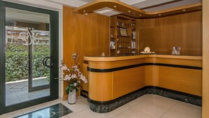 Un espace d’accueil avec un comptoir de r éception en bois, une porte vitrée donnant sur l’extérieur et un pot contenant une plante orchidée.