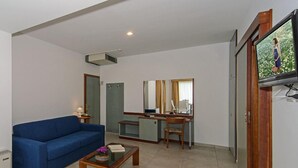 Un salon avec un canapé bleu, une table basse en bois, un bureau avec une chaise, une télévision et un miroir.
