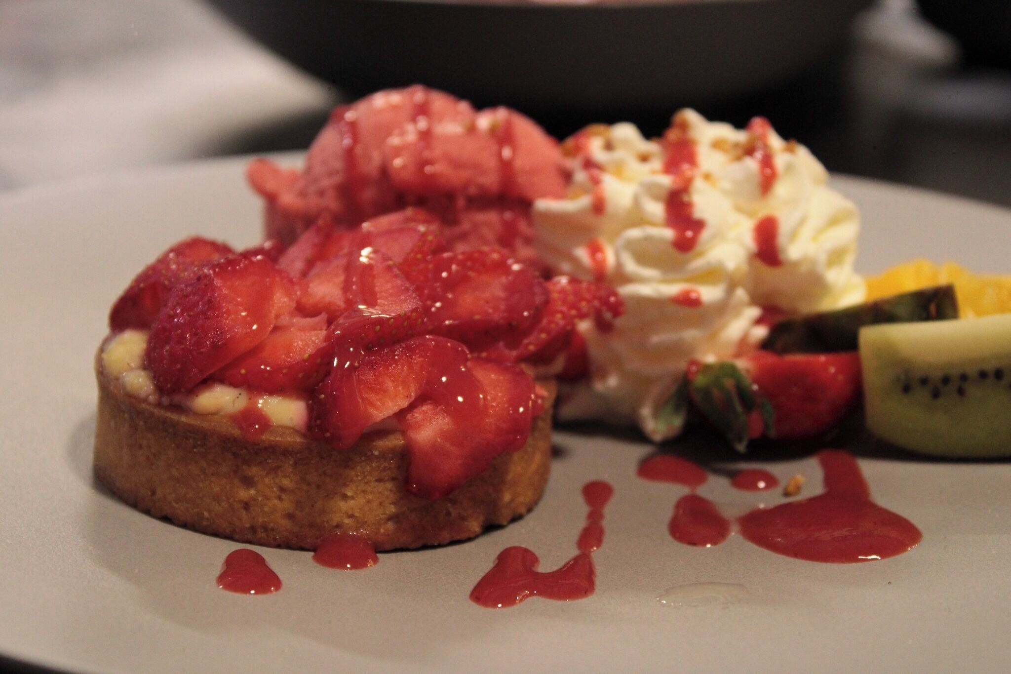 Une assiette à dessert avec une part de gâteau garnie de fraises et de crème fouettée, accompagnée d’une boule de glace et d’un morceau de kiwi.