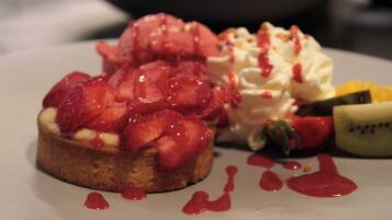 Une assiette à dessert avec une part de gâteau garnie de fraises et de crème fouettée, accompagnée d’une boule de glace et d’un morceau de kiwi.